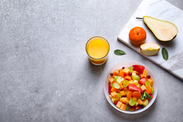 Bowl with fresh fruit salad and glass of juice on grey background