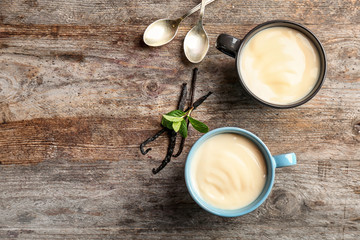 Cups with vanilla pudding, sticks and fresh mint on wooden background