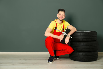 Male mechanic with car tires on color wall background