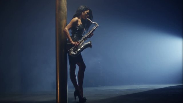 Young, beautiful, sexy, brunette woman dancing and playing golden saxophone on dark background . Shot in slow motion.