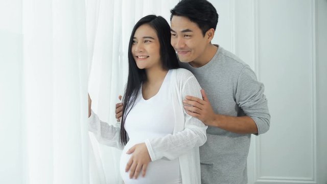 Young man and pregnant wife at the windows with curtains