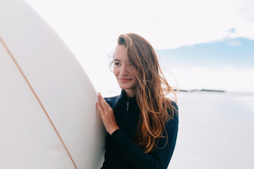 Surfer girl in sport swimwear posing with surfboard on the beach. Active lifestyle and summer vacations.Happy girl in bikini have fun before surfing Surfer lie on surf board, look at sunset sky