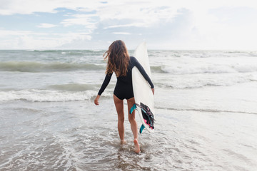 Young sporty active woman dressed swimsuit runs in the ocean with surf board in sunny day. Surfer...