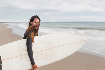 Young adorable woman with long hair and sportive tanned body, smiling and jogging with surf board on the beach in sunny summer day, ready for surfing. Wearing swimsuit - obrazy, fototapety, plakaty