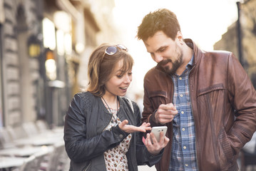 Cute young couple gossiping about some online content they're browsing on a cell phone, having fun together in an outdoor urban area