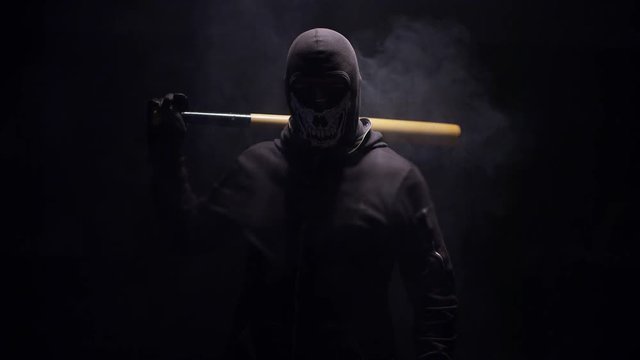 Portrait of masked hooligan with baseball bat on black background . Shot on RED cinema camera .