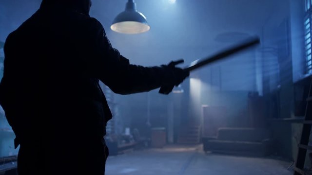 Masked bandit with baseball bat entering to the abandoned place. Shot on RED Cinema Camera in slow motion.