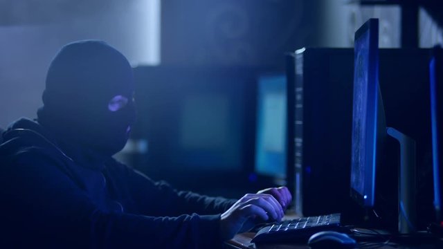 Hacker with mask breaking code. . Hacker with mask using laptop and computers to crack the internet from hackers dark room. Shot on RED Cinema Camera.