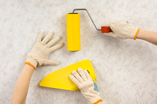 hands with spatula and roller smoothing wallpaper