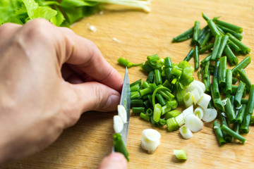 Woman hands holding knife chop on green onions.