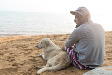 Man and dog sitting together on sand beach on vacation time, back view.