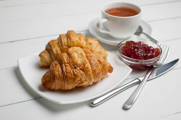 Croissants on a chopping board, strawberry jam and tea. Light breakfast