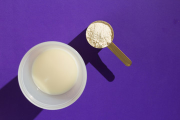 Whey Protein. Simplicity and hard light. Measuring scoop full with chocolate flavour powder and shaker with milk on violet background.