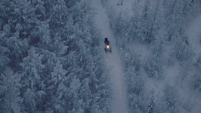 A snowmobile with a forester is riding through the woods at night 