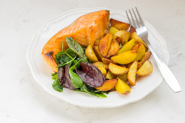 Fried potatoes with fish and green salad on a white plate