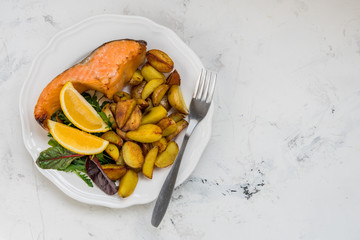 Fried potatoes with fish and green salad on a white plate
