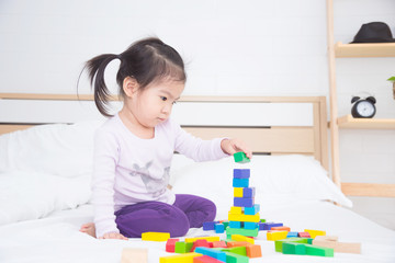 Little asian girl playing colorful wooden blocks on bed