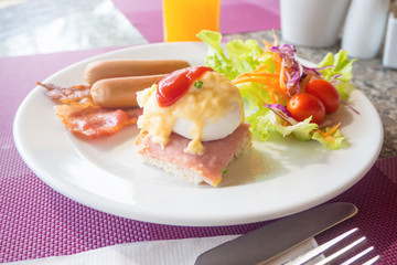 Egg benedict,bacon,sausages and salad on white plate
