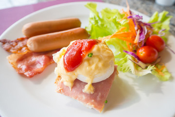 Egg benedict,bacon,sausages and salad on white plate