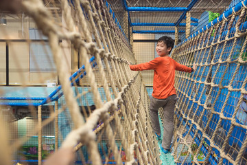 Young asian boy climbing rope at indoors playground