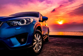 Fototapete Autos Blaues kompaktes SUV-Auto mit Sport und modernem Design, das bei Sonnenuntergang auf einer Betonstraße am Meer geparkt ist. Umweltfreundliche Technologie. Geschäftserfolgskonzept.