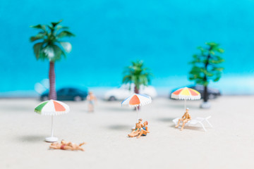 Fototapeta na wymiar Miniature people wearing swimsuit relaxing on the beach with blue background