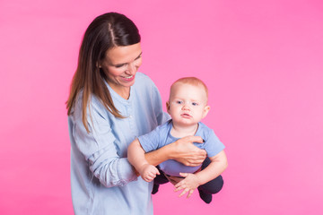 happy young mother with a baby child on pink background