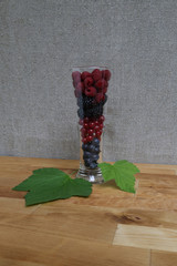 blueberries, redcurrants, blackberries, raspberry in a glass and currant leaves as decoration