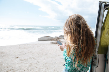 young woman whit her back to camera reading her mobile phone in front of a nice sea view