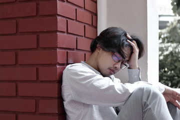 Sad stressed young Asian business man touching forehead with hands.