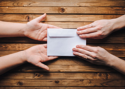 Hands pass the white envelope to the other hands on a wooden background. Transfer of money for donation. To send a letter.