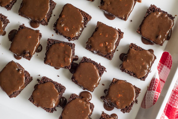 Chocolate brownies covered with chocolate nut ganache - Close up top view of brownie squares in white tray