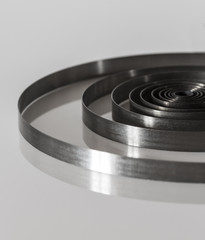 Spiral steel spring on a white mirror surface close-up.