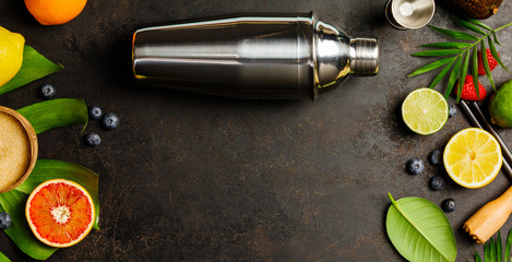 Cocktail shaker, tropical fruits and leaves on a dark background