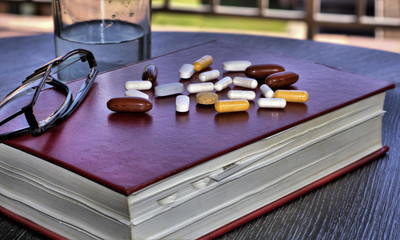 Medicine pills or drug pills with book. Close up of Medical tablets or drug tablets on book with reading glasses and glass of water.
