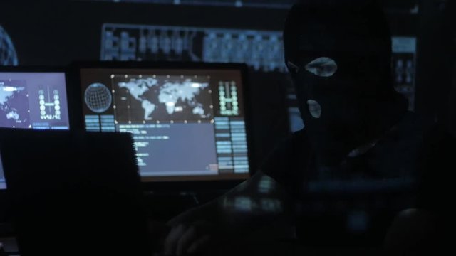 Dangerous hacker in the mask tries to enter the system using codes and numbers to find out the security password. The concept of cybercrime.