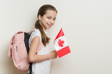 Schoolgirl 10 years in white T-shirt with a backpack holding the flag of Canada