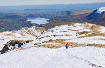 A female hiker descending from a snow covered Place Fell summit in the English Lake District.