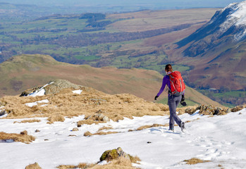 A female hiker descending from a snow covered Place Fell summit in the English Lake District.