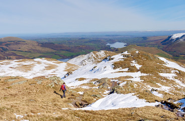 A female hiker descending from a snow covered Place Fell summit in the English Lake District.
