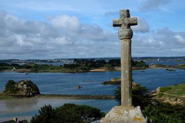 stony historic cross on a blue sky with countryside and the bay