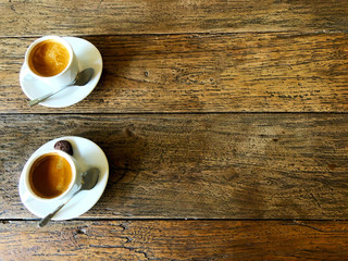 Two cups of strong black coffee stand side by side on a wooden table in a cafe.