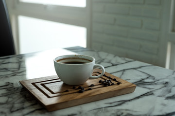 Closeup image of a cup of hot coffee and a wooden saucer on the table in cafe