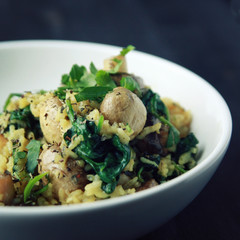 Yellow rice with mushrooms and spinach. Vegan dish. European cuisine. Vegetarian turmeric rice in the white bowl. Meatless. Toned photo.