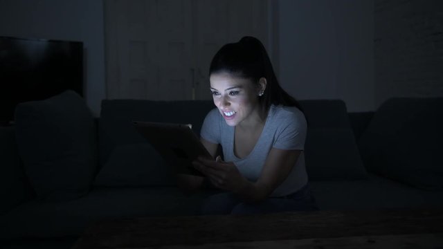 lateral pan shot of young beautiful happy and relaxed latin woman 30s lying on home couch late night using digital device laptop tablet pad 