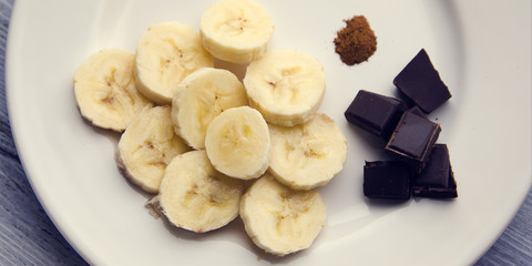 Dark chocolate, banana and cinnamon. Ingredients for a smoothie on the white plate. Top view photo.