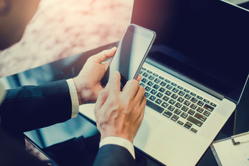 close up of businessman hand typing on smart phone with labtop in office
