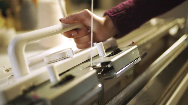 Female hands making knitted texture on weaving machine. Close up process manufacturing textile on knitting machine at modern factory. Handmade weaving fabric on loom machine