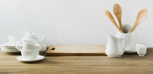 White kitchen utensils, dishware and other different white stuff for serving on white wooden board.
