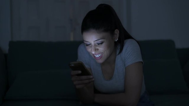 young attractive and relaxed hispanic 30s woman with mobile phone smiling happy using dating app late night in internet social media addiction concept
